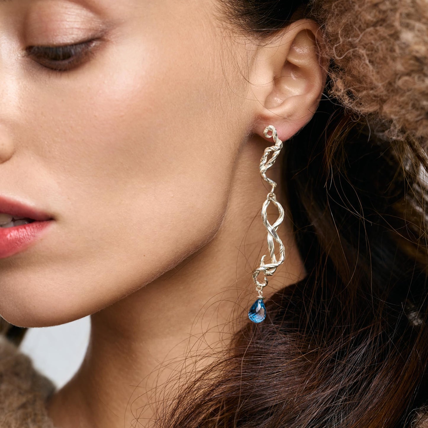Model wearing Rawan Kanan long handcrafted sculptural 925 silver earrings with blue topaz gemstone drops.