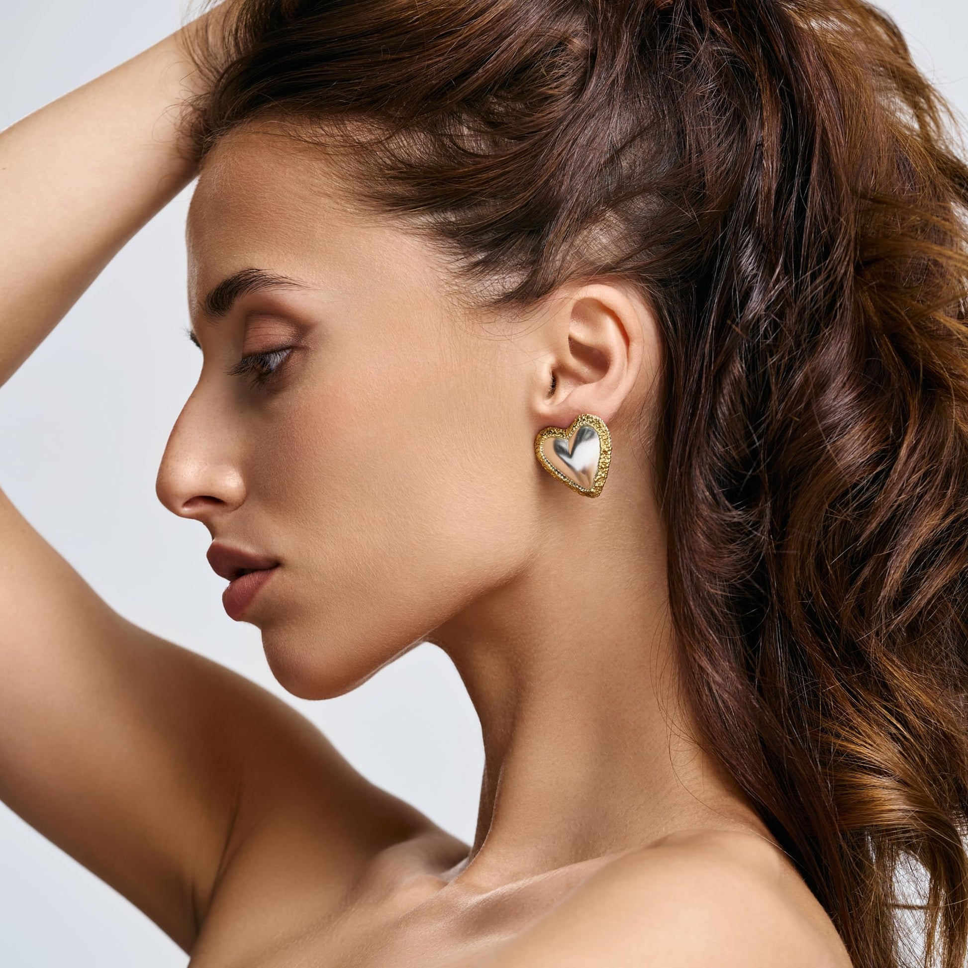 Model wearing Rawan Kanan handcrafted two-tone heart stud earrings in 925 silver and textured 14K gold frame.
