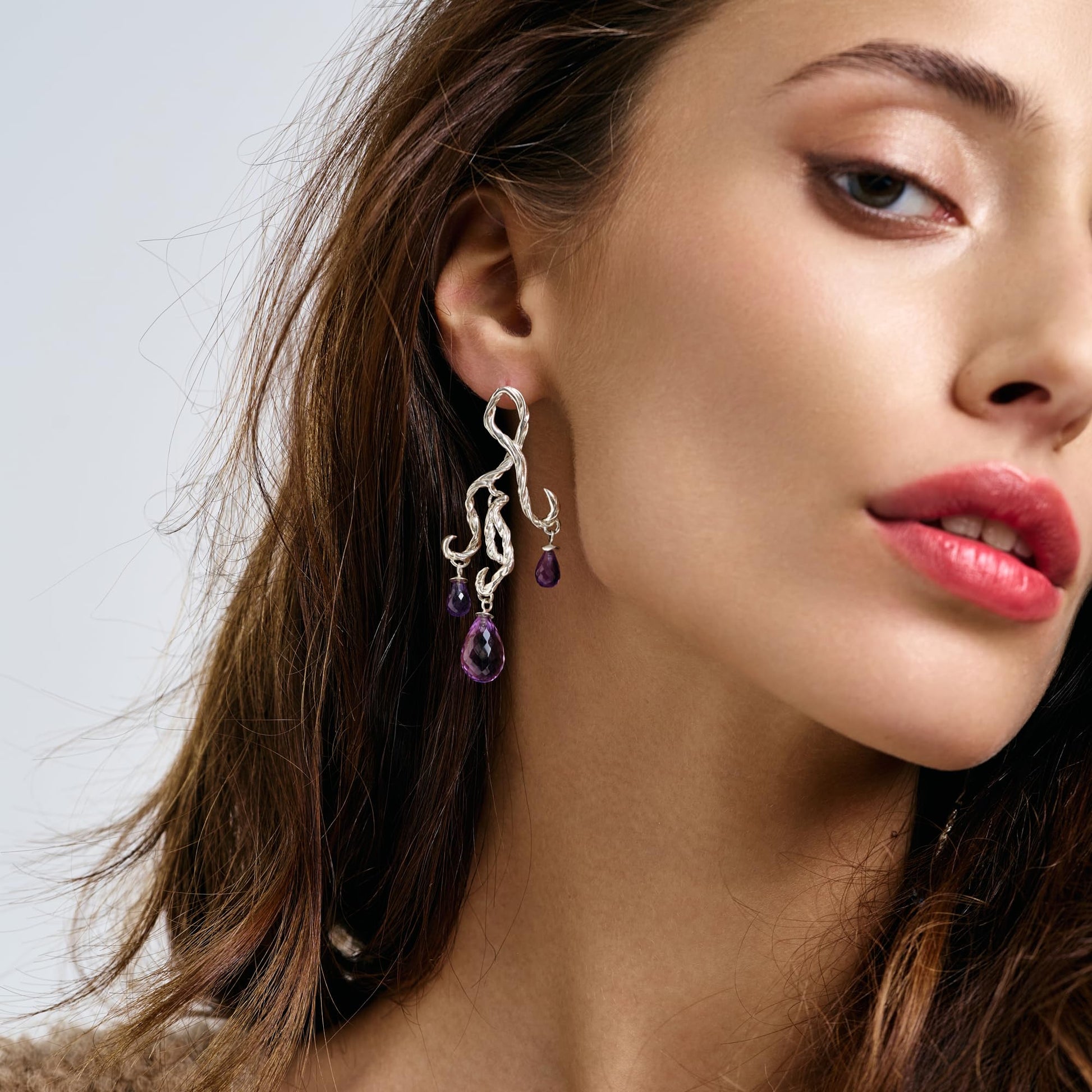 Model wearing Rawan Kanan handcrafted sculptural chandelier earrings in 925 silver with purple amethyst gemstone drops.
