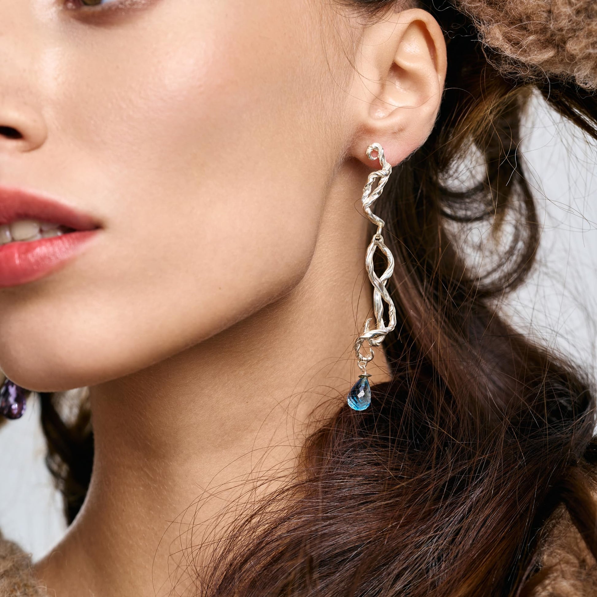 Model wearing Rawan Kanan long handcrafted sculptural 925 silver earrings with blue topaz gemstone drops.