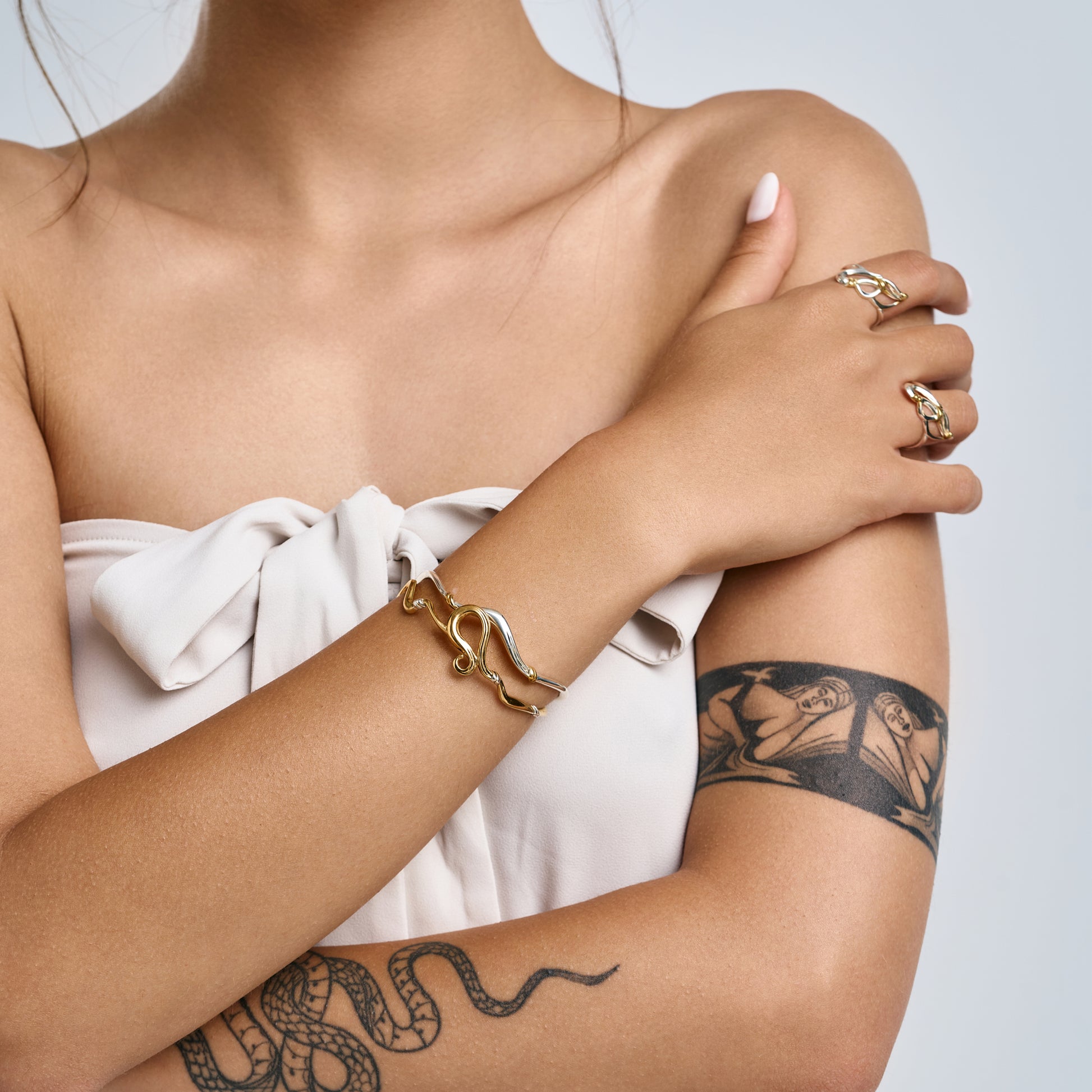 Hand of a woman wearing a delicate silver wave bracelet and matching organic rings, showcasing minimalist luxury jewelry styling.