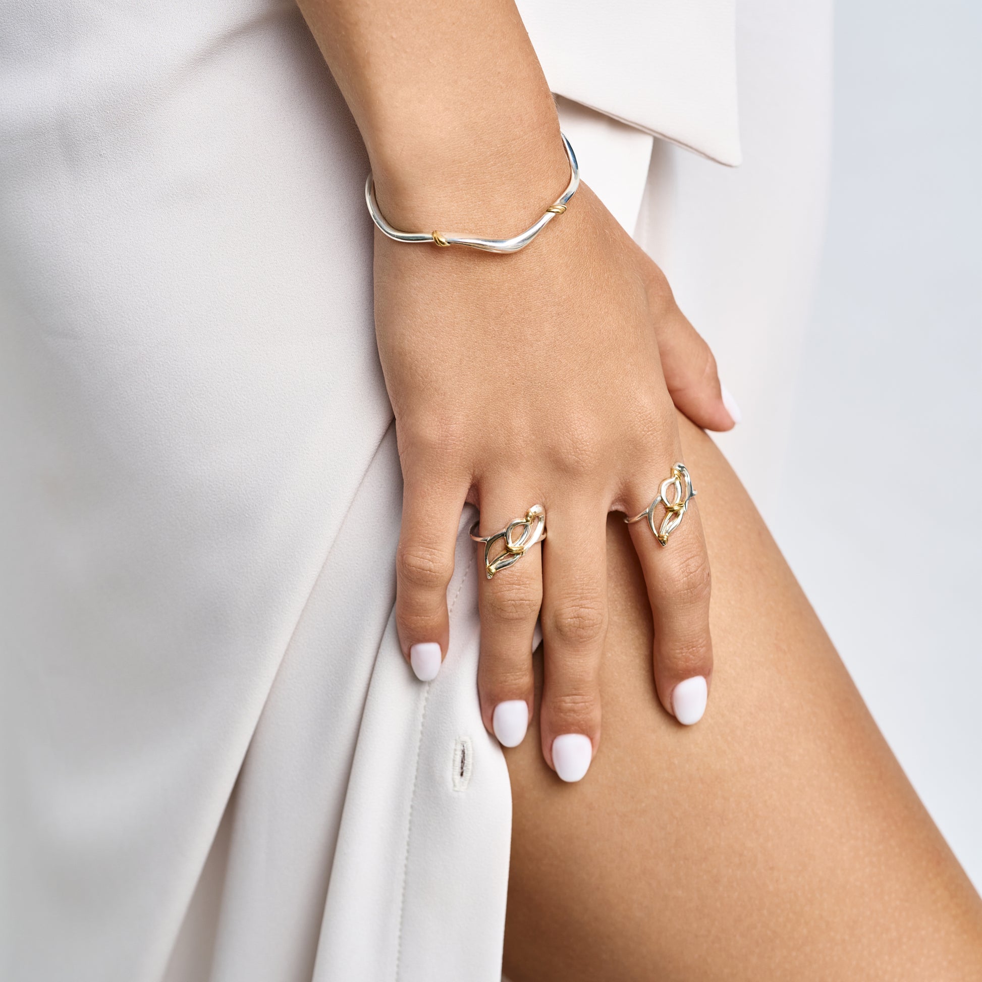 Hand of a woman wearing a delicate silver wave bracelet and matching organic rings, showcasing minimalist luxury jewelry styling.